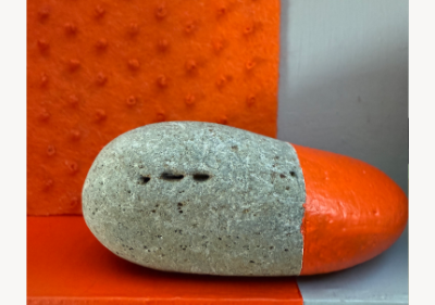 Wall-mounted assemblage split orange and gray, with a deep recessed box lined in orange textured felt and gray-painted wood, holding a stone painted half orange and half left its natural gray.
