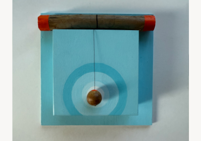 Wall-mounted assemblage of light blue painted wood, with a weathered branch capped in orange resting across the top and a small oak gall hanging by black thread over a hand-painted blue target.