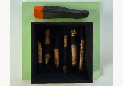 Wall-mounted assemblage on pale green wood, with a charred branch capped in orange resting above a black recessed box holding six upright sticks painted black and natural wood in bands.