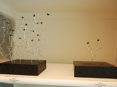 Two wire-and-wax sculptures with stemmed forms mounted on black bases, titled and labeled