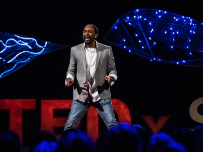 A performer on the TEDxSalem stage, with two of the overhead sculptures lit blue behind him