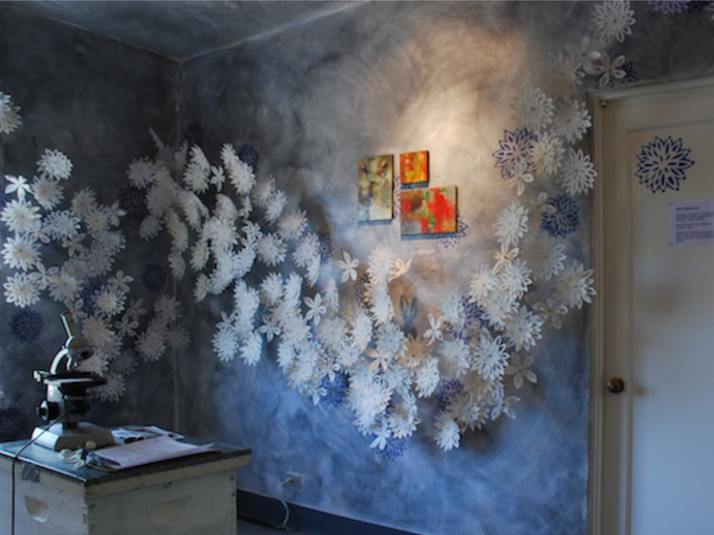Wax paper flower cascade beside a doorway with three encaustic paintings, See installation entry