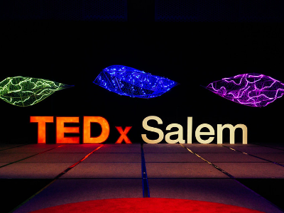 The three overhead sculptures lit green, blue, and purple above the empty TEDxSalem stage
